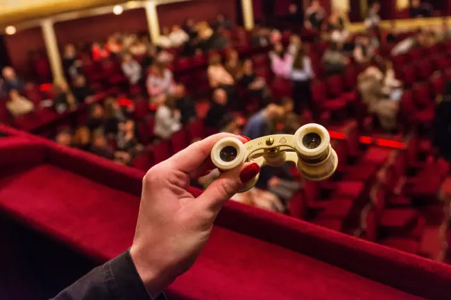 Person in einer Oper hält Elfenbein Ferngläser