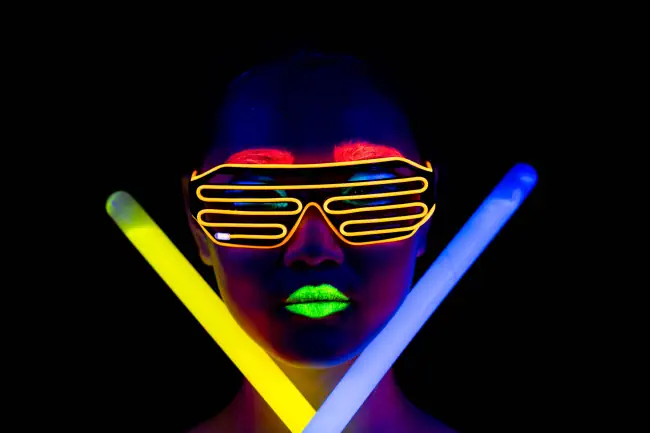 Schöne sexy Frau mit UV-Farbe im Gesicht, leuchtende Kleidung, leuchtendes Armband vor der Kamera.