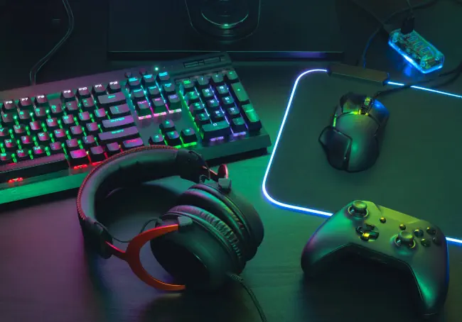 Gaming Equipment. Draufsicht einer Maus, Tastatur, Joystick, Headset, Handystick, Handy-Joystick, Kopfhörer und Mauspad mit Farbton auf schwarzem Tischhintergrund.