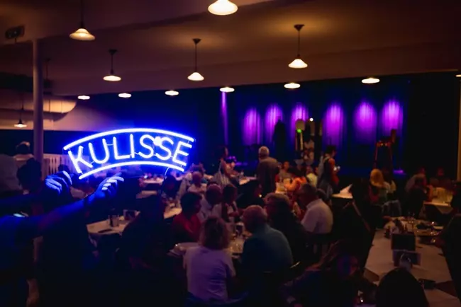 Publikum sitzt in der Kulisse Wien, während im Vordergrund das hell leuchtendes Logo zu sehen ist.